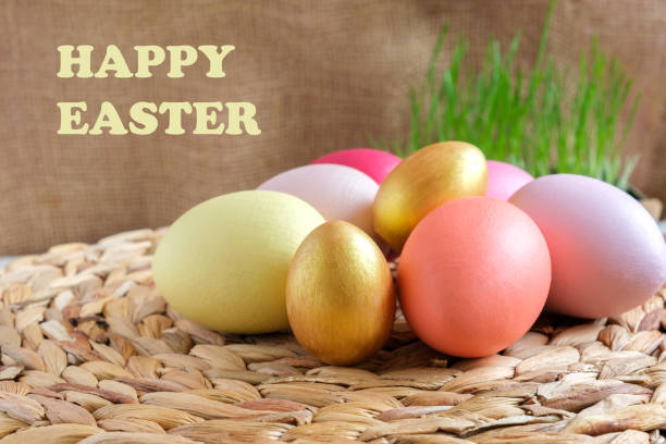 Easter colorful eggs in a basket on white wooden table. Burlap background. Rustic, Eco concept. Dyed Eggs on a straw Napkin. Easter Centerpieces. Text Happy Easter