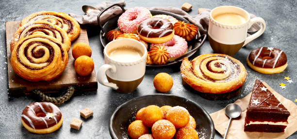 Table with various cookies, donuts, cakes and coffe cups on dark backround. Panorama