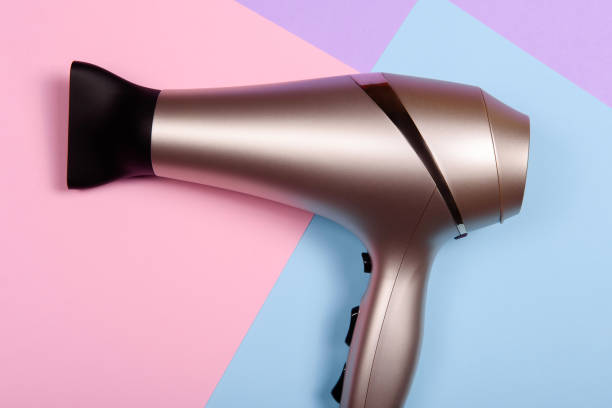 Golden hair dryer on pink, blue and purple paper background, copy space. Top view, flat lay stock photo