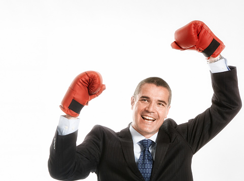 It takes a fight to succeed in business: man in a smart suit, wearing boxing gloves, punching the air to celebrate his success.