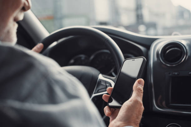 istock Man looking at mobile phone while driving a car. Old pensioner person distracting texting and chatting. 1371746624