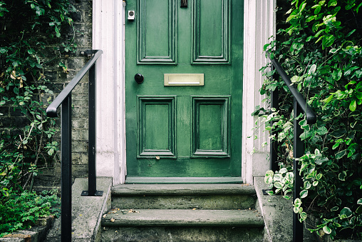 Traditional green-painted wooden door with traditional, victorian styled steps leading to the front of a terraced victorian house in a mews area of London.