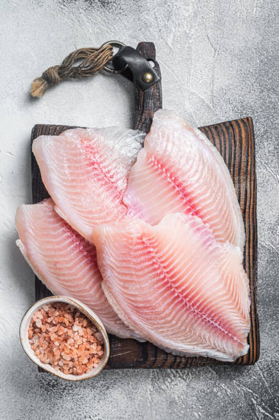 istock Uncooked tilapia fish fillet on a wooden board. White background. Top view 1371747228