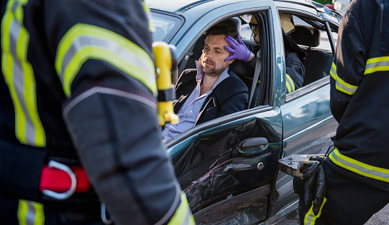 Shot of a firefighter opening door with clamp to rescue a driver from a damaged car. Saving lifes and saftey concept.