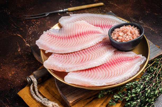 filetto di pesce crudo di tilapia in un piatto con spezie. sfondo scuro. vista dall'alto - pepper pink red white foto e immagini stock