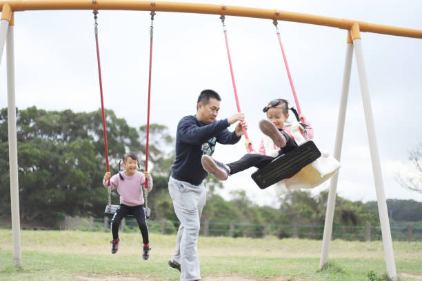 istock a father playing swings with his twin daughters. 1371748569