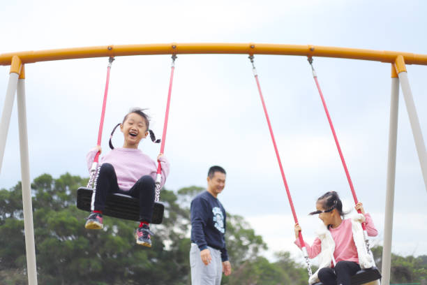 istock a father playing swings with his twin daughters. 1371748751