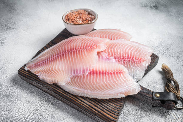 istock Uncooked tilapia fish fillet on a wooden board. White background. Top view. 1371748986