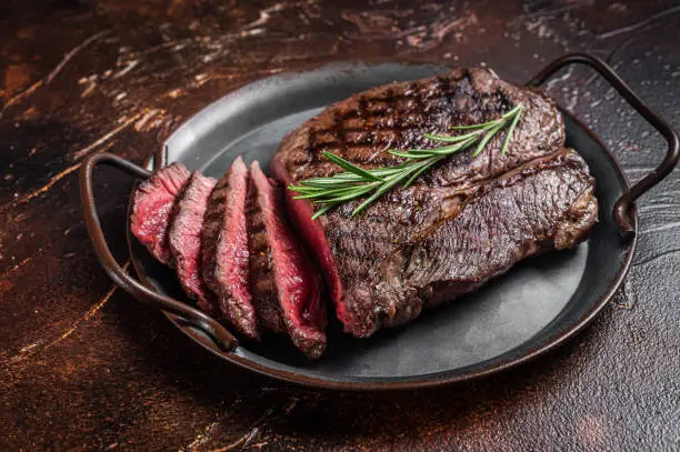 Photo of Grilled Medium Rare top sirloin beef steak or rump steak on a steel tray. Dark background. Top view