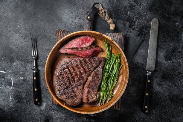 bbq grilled medium rare top sirloin beef steak, rump steak in a wooden plate. black background. top view - circular skirt fotos imagens e fotografias de stock