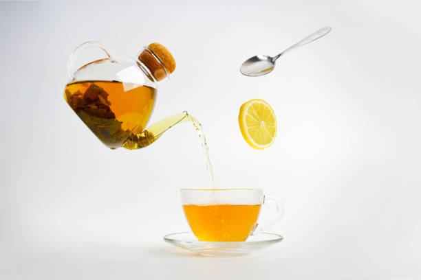 Tea pours out of a transparent kettle into a transparent cup. Lemon slice and spoon fall down