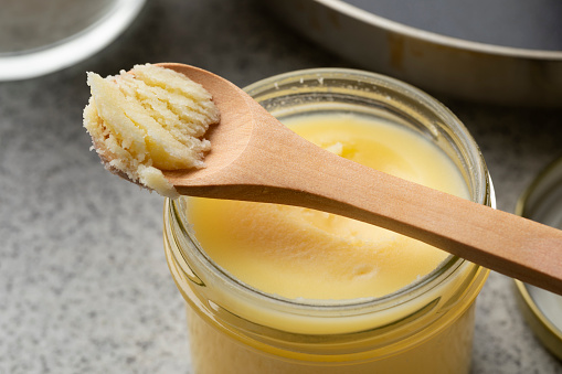 Glass jar and wooden spoon with yellow ghee close up