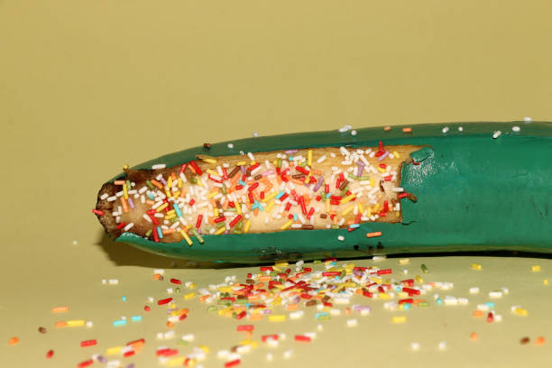 a green banana that has a decorative sugar color on a peeled part on a yellow background