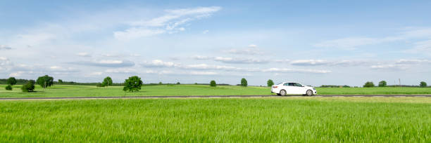 istock Small passenger car driving through green countryside meadow 1371757693