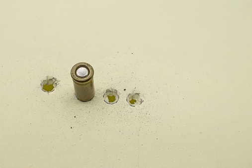 Four bullets holes of 6.35 mm caliber on a yellow cardboard with traces of powder and an embedded bullet