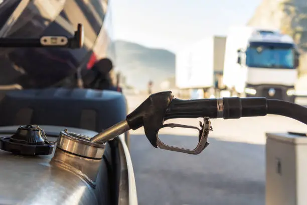 Truck refueling diesel at a highway gas station, close-up of the nozzle inserted in the vehicle's tank.