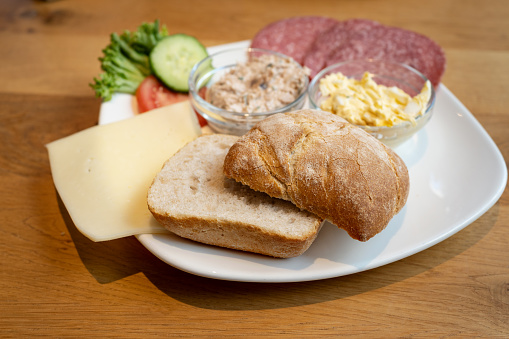 German breakfast plate with crispy bread roll, cheese, sausage and creamy spreads on a wooden table, selected focus, narrow depth of field