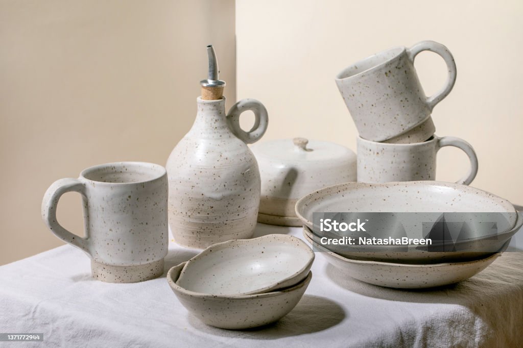 Set of empty craft ceramic speckled bowls Set of empty craft ceramic tableware, white speckled bowls, plates, mugs and oil bottle standing on white table cloth. Ceramics Stock Photo
