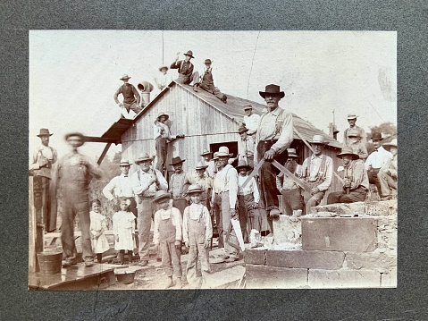 1898 photograph of men and children taking a photo break from building a barn. Pencil lines identify certain people.
