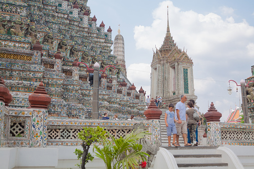 Tourists at Wat Arun in Bangkok. Several groups of temple are walking around huge pagoda. In foreground are a mature man and a boy