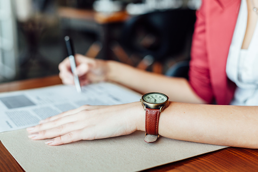 Woman signing contract with leather wristwatch in close up.