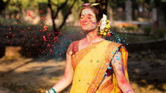 Holi festival of color, Splashing dry organic color or colour or gulal or abeer or Holi powder on a beautiful young girl woman lady in indian attire saree playing celebrating enjoying holi