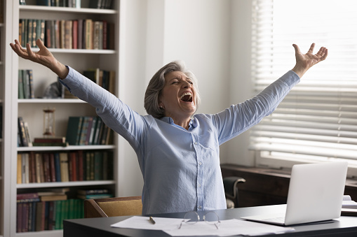 Overjoyed happy middle aged 60s woman screaming with raise in air arms, getting email with amazing news, celebrating online lottery gambling win, getting bank loan approval, internet success.