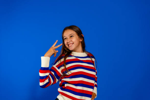 photo of young funny preteen girl happy positive smile show peace v-sign isolated over blue color background - offspring child toothy smile beautiful imagens e fotografias de stock