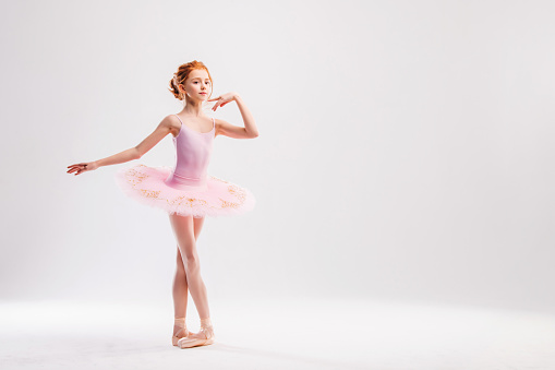 Beautiful female ballet dancer on a grey background. Ballerina is wearing a white tutu and pointe shoes.