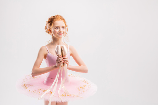 Portrait of little tender red-haired girl in pink tutu with pointe shoes, dreaming of becoming ballerina