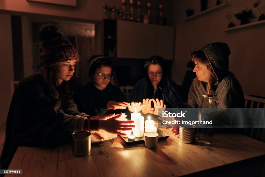 Family sitting by the candles during the blackout. During the energy crisis family is sitting by the table, lit by candles. Everyone is wearing warm clothes because of heating problems during the power outage. They are eating dry biscuits and warming hands from the candle flame.
Canon R5 Blackout Stock Photo