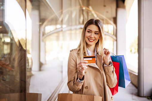 Smiling young woman is posing with a credit card and shopping bags