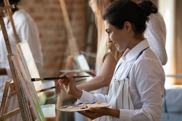 Happy young Indian woman drawing on easel in studio.