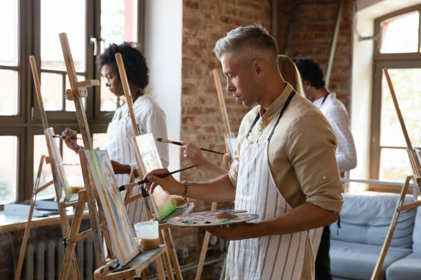 istock Concentrated young handsome man drawing on easel in studio. 1371797954