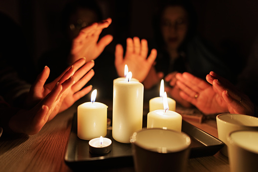 During the energy crisis family is sitting by the table, lit by candles. Everyone is wearing warm clothes because of heating problems during the power outage. They are warming hands from the candle flame.\nCanon R5