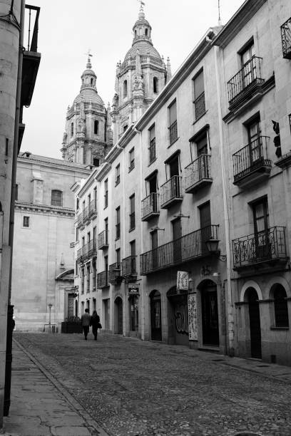 Salamanca, Spain, 4th April 2018. A couple walking through the old part of the town. At the end of the street, the Pontifical University with the Clerencia tower. Shoot in black and white.