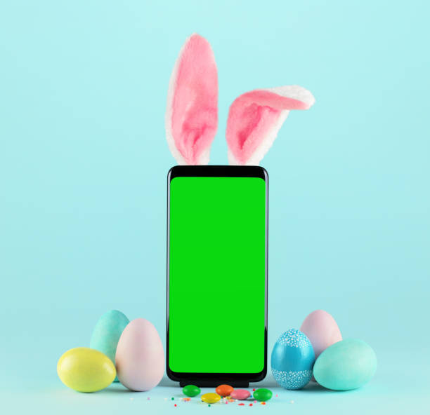 Smartphone with green screen and Easter Bunny ears surrounded by painted eggs on blue background