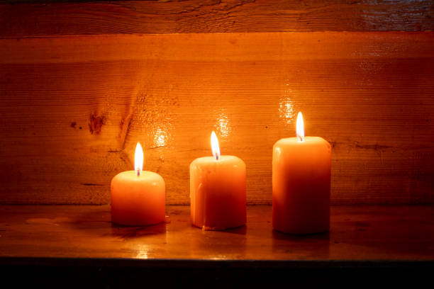 Three lit orange candles on a wooden background close-up