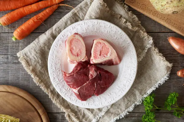 Ingredients for preparing a beef broth or soup - marrow bones, meat and fresh vegetables, top view