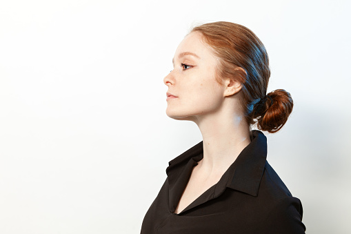 Close-up studio portrait of an attractive 20 year old red-haired woman in a black shirt on a white background