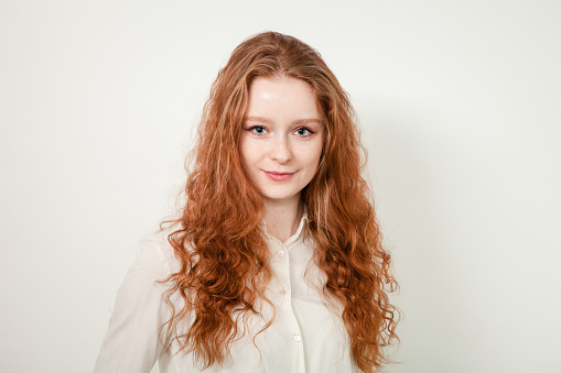 Authentic brunette young woman dressed in white three-quarter sleeve fur coat and light pink scarf on head looking at camera on winter day outdoors. Shallow depth of field, selective focus foreground. Part of series of photos