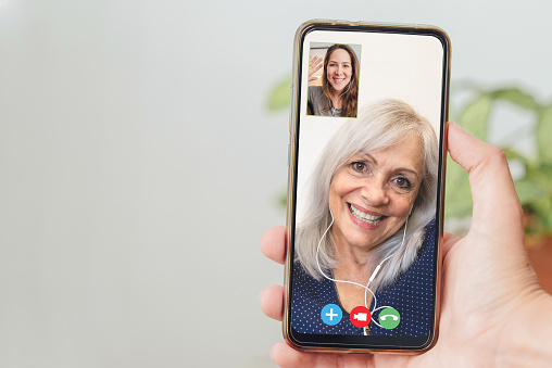 Happy senior and daughter talking on video call with mobile phone - Focus on hand holding smartphone