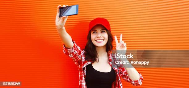 Summer Portrait Of Happy Smiling Young Woman Taking Selfie By Smartphone Wearing Baseball Cap On Red Background Stock Photo - Download Image Now