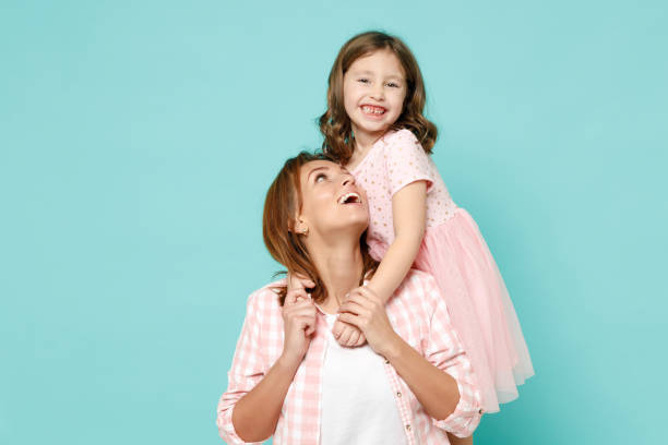 happy woman in pink clothes have fun with child baby girl 5-6 years old mommy little kid daughter stand behind hug kiss isolated on pastel blue azure background studio mothers day love family concept - family child portrait little girls imagens e fotografias de stock