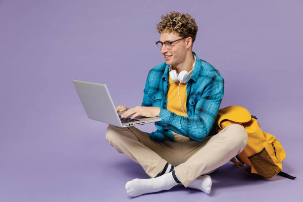 Full body young boy teen student in casual clothes backpack headphones glasses sit hold work laptop computer isolated on violet background studio Education in high school university college concept Full body young boy teen student in casual clothes backpack headphones glasses sit hold work on laptop computer isolated on violet background studio Education in high school university college concept isolated color stock pictures, royalty-free photos & images