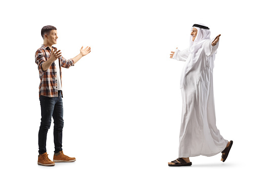 Full length profile shot of an arab man walking with open arms towards a casual young man isolated on white background