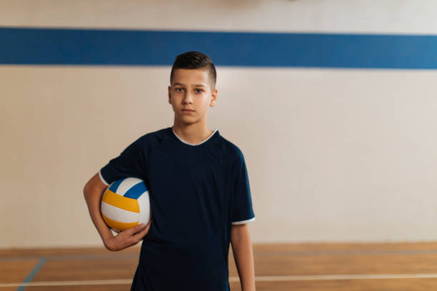 Boy with a volleyball Boy is standing in the volleyball hall on the floor, looking at the camera and holding the ball in his hand male volleyball player stock pictures, royalty-free photos & images