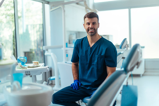 Portrait shot of a young smiling dentist sitting in his clinic