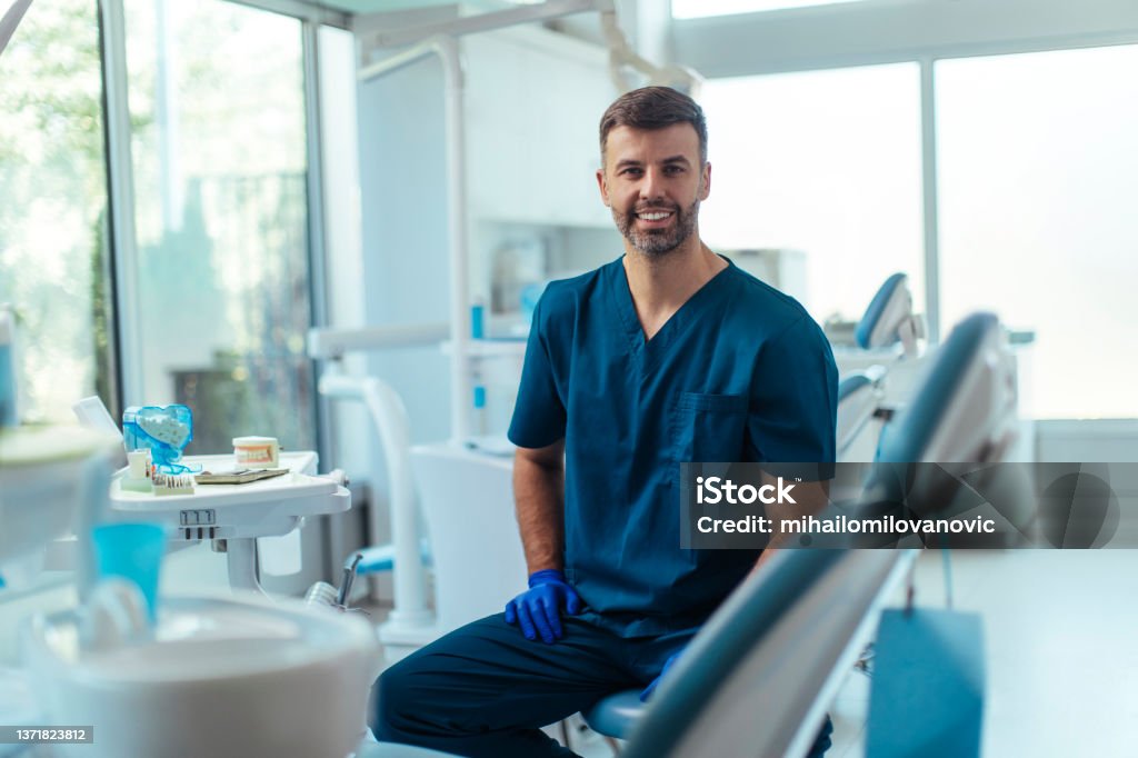 He loves making his clients happy Portrait shot of a young smiling dentist sitting in his clinic Dentist Stock Photo