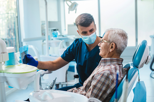 Senior man sitting in a dental chair while his dentist reads him out an x-ray scan